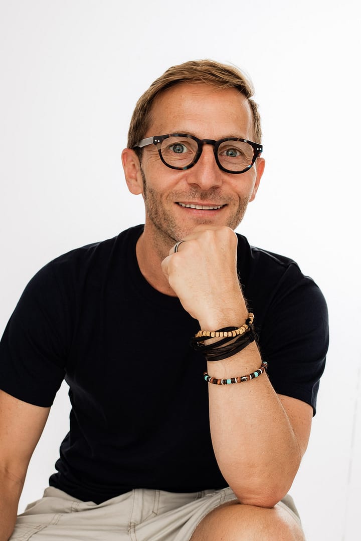 The author of this blog, Francois is wearing a black t-shirt , is having short hair blond and glasses, and posing to a camera with his hand with bracelets on his chin